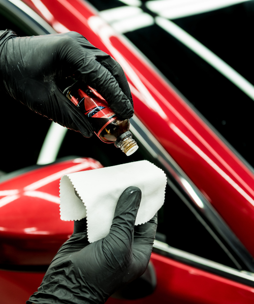 A person cleaning a red car with a cloth